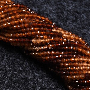 May include: A strand of brown faceted gemstone beads. The beads are small and round, and they have a shiny, polished finish.