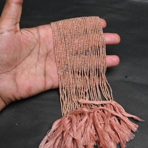 May include: A collection of small, peach-toned beads on strings, with a matching tassel. The beads are closely strung, creating a shimmering appearance. The tassel is made of multiple threads, adding texture. Suitable for jewellery making.