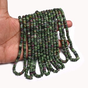 May include: A long strand of small, flat, circular disc-shaped beads. The beads feature a mottled pattern of deep forest green, dark black, and vibrant magenta pink tones, arranged in multiple parallel vertical rows on a white background.