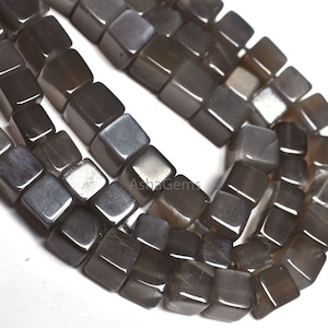 Può includere: Una collana di perle di pietra preziosa grigio scuro, ogni perla ha una forma cubica con una finitura liscia e lucida.