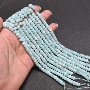 Puede incluir: Una hebra de cuentas de piedras preciosas facetadas de color azul claro. Las cuentas son pequeñas y redondas, y están enhebradas en un alambre fino. Las cuentas están dispuestas en línea recta, y todas son del mismo tamaño y forma.