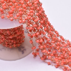 Peut inclure: Un long brin de perles de corail et de chaîne dorée, enroulé autour d'une bobine blanche. Les perles sont d'une couleur rose-orange vibrante et la chaîne est d'un or brillant.