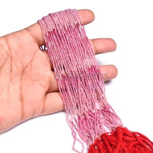 Könnte beinhalten: Ein langer Strang aus winzigen, facettierten rosa Edelsteinperlen, die in einem Farbverlauf von hellem Pastellrosa bis zu tiefem Magenta angeordnet sind. Die Perlen sind auf mehrere dünne Fäden gezogen, die in einer roten Quaste enden.