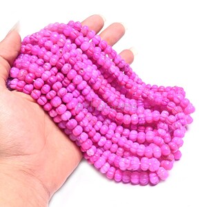 Puede incluir: Un puñado de vibrantes cuentas rosas. Las pequeñas cuentas redondas tienen forma de flor. Están ensartadas, creando una apariencia fluida y texturizada. El color rosa brillante es consistente en todos los hilos, ofreciendo un aspecto llamativo.
