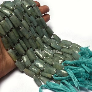 Puede incluir: Una hebra de cuentas de piedra preciosa de aguamarina verde claro, facetadas y de forma rectangular, con cuentas espaciadoras plateadas. Las cuentas están enhebradas en un cordón con borlas turquesas en el extremo.