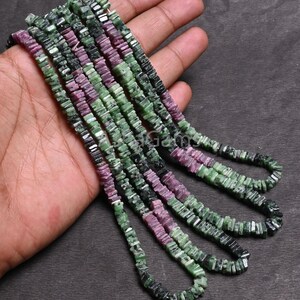 May include: A strand of green and pink gemstone beads, with a square shape, are strung together on a wire. The beads are arranged in a repeating pattern of green and pink.