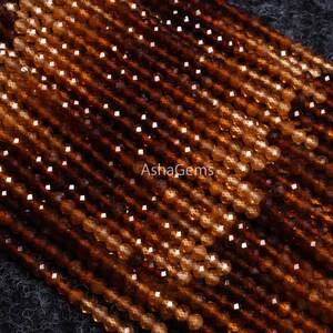 May include: A strand of brown and orange gemstone beads. The beads are faceted and have a shiny finish. The beads are arranged in a diagonal pattern.