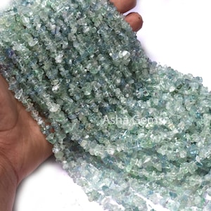 May include: A strand of light green and blue aquamarine chip beads. The beads are irregular in shape and have a translucent appearance.