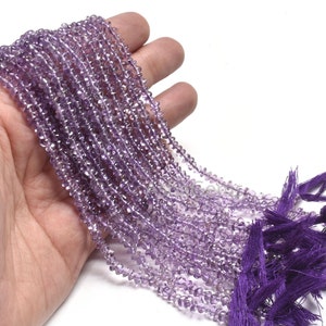 Puede incluir: Una hebra de cuentas de piedra preciosa de amatista, facetadas y enhebradas en un hilo fino. Las cuentas son de color púrpura claro y tienen un ligero brillo. La hebra mide aproximadamente 40 cm de largo y está terminada con un borla.
