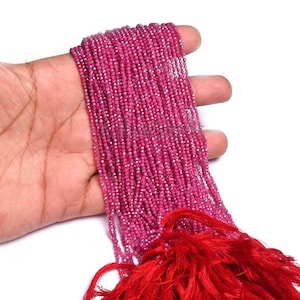 Peut inclure: Un long chapelet de petites perles de rubis facettées rose foncé, disposées en plusieurs rangées parallèles. Les perles ont une surface réfléchissante et scintillante, et sont rassemblées en bas par un pompon rouge vif en fil fin.