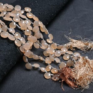 Puede incluir: Una hebra de cuentas de piedras preciosas de color rosa claro con forma de lágrima facetada. Las cuentas están enhebradas en un alambre plateado y tienen una apariencia natural y translúcida.