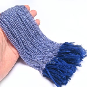 Puede incluir: Una hebra de cuentas de piedras preciosas de color azul claro con un borla azul. Las cuentas son peque&ntilde;as y redondas, y la borla est&aacute; hecha de un material suave y esponjoso.