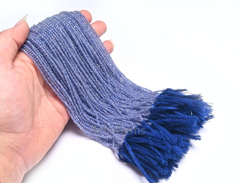 Puede incluir: Una hebra de cuentas de piedras preciosas de color azul claro con un borla azul. Las cuentas son peque&ntilde;as y redondas, y la borla est&aacute; hecha de un material suave y esponjoso.