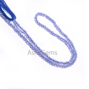 Puede incluir: Una hebra de cuentas de piedras preciosas de color azul claro, enhebradas en un hilo azul. Las cuentas son facetadas y tienen un ligero brillo iridiscente.