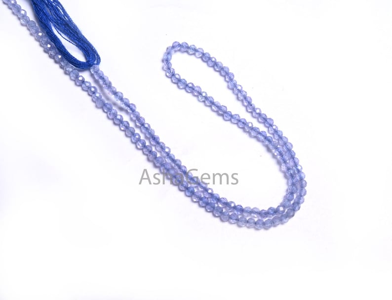Puede incluir: Una hebra de cuentas de piedras preciosas de color azul claro, enhebradas en un hilo azul. Las cuentas son facetadas y tienen un ligero brillo iridiscente.