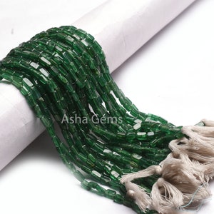 May include: A collection of green, rectangular beads with a glossy finish. The beads are strung together and finished with a tassel. The text "Asha Gems" is visible on the image.