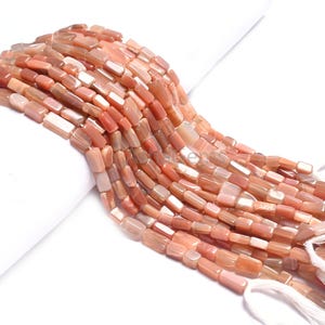 Puede incluir: Una hebra de cuentas de piedra de sol de forma rectangular. Las cuentas son una mezcla de naranja claro y oscuro con un acabado brillante.