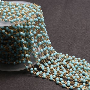 May include: A long strand of light blue faceted beads strung on a gold chain. The beads are small and uniform in size. The chain is delicate and has a subtle shine.