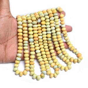 Pode incluir: Fios de contas de pedras preciosas amarelas. As contas são ovais e têm uma superfície lisa e polida. A cor varia do amarelo pálido a um tom dourado mais profundo, com toques de verde e laranja. As contas são enfiadas.