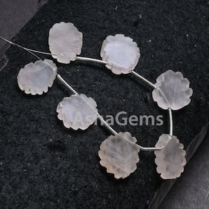 Könnte beinhalten: Eine Strähne aus rosafarbenen Rosenquarzperlen mit einem facettierten, blumenförmigen Design. Die Perlen sind auf einem Silberdraht aufgefädelt.