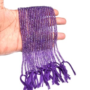 Peut inclure: Plusieurs brins de petites perles violettes à facettes, chacune avec un aspect scintillant. Les perles sont maintenues ensemble et finies avec un pompon violet assorti. Ces perles sont probablement destinées à la fabrication de bijoux ou à l'artisanat.