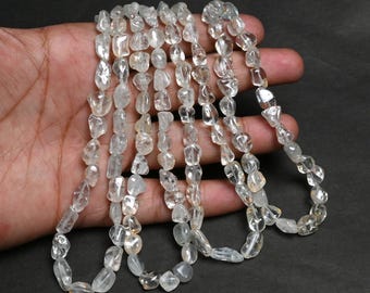 May include: A necklace of clear, irregular-shaped gemstones. The stones are strung together, creating a strand of varying sizes and shapes. The gemstones have a translucent quality, with a slight shimmer. The necklace is displayed against a dark background.