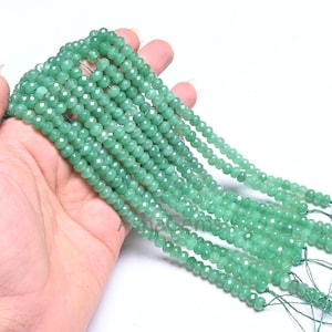 May include: A strand of green faceted gemstone beads. The beads are small and round, and they are strung on a thin thread. The beads are arranged in a long, flowing strand.
