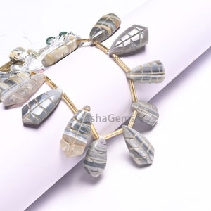 Peut inclure: Un brin de perles de pierre d'agate rayée grise et blanche avec un motif de feuille sculpté. Les perles sont enfilées sur un fil de couleur or.