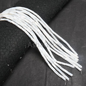 Puede incluir: Una hebra de cuentas blancas de madreperla, cada cuenta tiene una forma rectangular alargada.