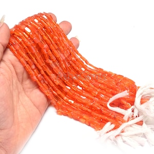 Könnte beinhalten: Eine Strähne orangefarbener Karneolperlen, jede Perle hat eine rechteckige Form mit abgerundeten Kanten. Die Perlen sind auf einer weißen Schnur aufgefädelt und mit einem weißen Knoten zusammengebunden.