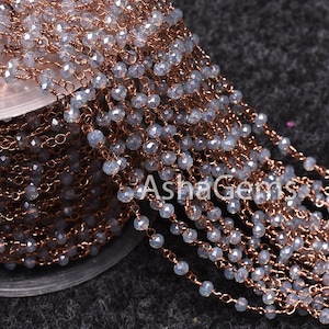 May include: A close-up of a silver and rose gold chain with faceted beads. The chain is wound around a spool. The chain is made of metal and beads.