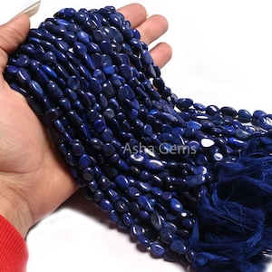 Peut inclure: Un brin de perles de lapis-lazuli bleu foncé, chaque perle est de forme ovale irrégulière et lisse. Les perles sont enfilées sur un fil bleu et ont un pompon bleu à l'extrémité.