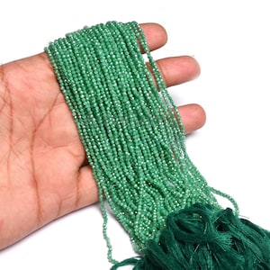 Puede incluir: Hebras de pequeñas cuentas verdes facetadas. Las cuentas se sostienen en una mano, con una borla verde oscuro en la parte inferior. Las cuentas tienen un ligero brillo y son de un tono verde vibrante.