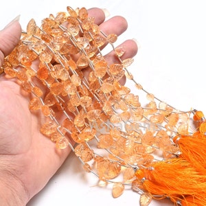 May include: A strand of orange gemstone beads in a leaf shape. The beads are strung on a silver wire and have a clear, translucent appearance.