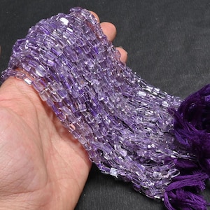 May include: A strand of amethyst gemstone beads, each bead is a rectangular prism with a light purple color. The beads are strung on a thread and are ready to be used for jewelry making.