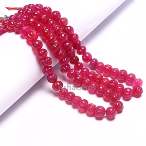 Può includere: Una collana di perline di pietra preziosa intagliata di colore rosa brillante. Le perline sono rotonde e hanno una superficie testurizzata. Le perline sono infilate su un filo trasparente.