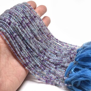 May include: A strand of light blue and purple round beads with a tassel on the end. The beads are small and uniform in size.