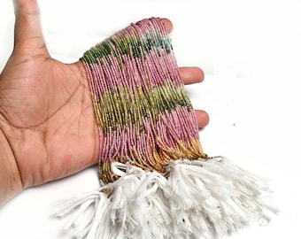 May include: A collection of multiple strands of small, faceted gemstone beads in a gradient of pink, yellow, and green hues. The strands are gathered together and secured at the bottom with white thread tassels, creating a long, flowing display.