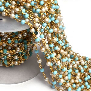 May include: A gold chain with alternating light blue and white beads. The chain is wound around a spool.