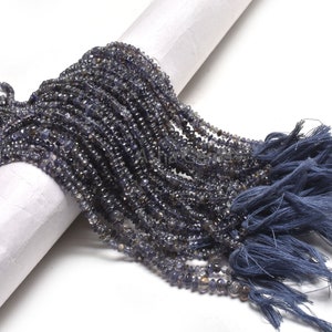 Pode incluir: Um fio de contas de pedras preciosas azul escuro, provavelmente cianita, com um tassel na ponta. As contas são pequenas e facetadas, criando um efeito brilhante.