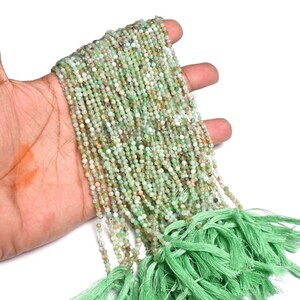 Pode incluir: Um longo fio de pequenas contas de pedras preciosas facetadas em tons de verde claro e pêssego pálido, dispostas em várias fileiras paralelas, terminando numa borla de tecido verde claro feita de numerosos fios finos e macios.