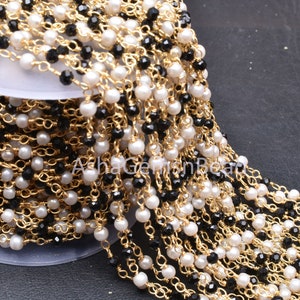 Peut inclure: Une chaîne dorée avec des perles blanches et noires. La chaîne est composée de petites perles rondes et est parfaite pour la fabrication de bijoux.