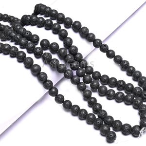 Puede incluir: Cadenas de cuentas negras de roca volcánica. Las cuentas son redondas y tienen una textura porosa. Las cuentas están ensartadas, para un collar o pulsera. Las cuentas son de color carbón oscuro.