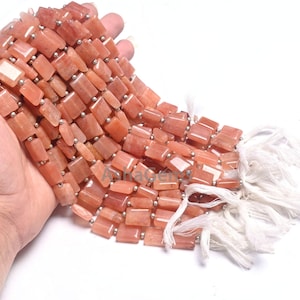 Puede incluir: Una hebra de cuentas de piedras preciosas de color melocotón, cada cuenta es rectangular y tiene un acabado liso y pulido. Las cuentas están enhebradas en un alambre de plata y tienen borlas blancas en el extremo.