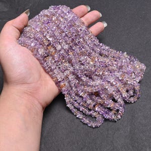 Könnte beinhalten: Eine Ansammlung mehrerer Stränge aus kleinen, unregelmäßigen, getrommelten Amethyst-Edelsteinsplittern. Die Perlen weisen durchscheinende Schattierungen in hellem Violett, Purpur und gelegentliche Einschlüsse von blassem Gelb oder klarem Quarz auf.