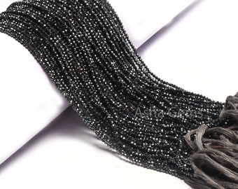 May include: A close-up of a large bundle of small, black, faceted beads. The beads are strung together, creating a flowing, textured appearance. The beads are on a white surface with a gray tassel.