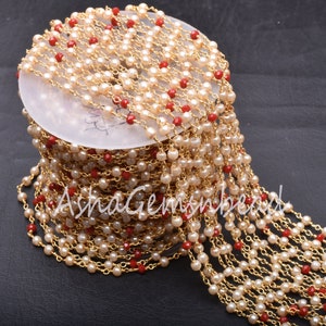 Könnte beinhalten: Eine Spule mit einer goldenen Kette mit weißen und roten Perlen. Die Kette besteht aus kleinen, miteinander verbundenen Metallteilen. Die Perlen sind rund und gleichmäßig auf der Kette verteilt.