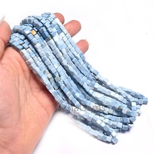 Könnte beinhalten: Eine Strähne aus hellblauen, quadratischen Opalperlen. Die Perlen sind etwa 6 mm groß und haben eine glatte, polierte Oberfläche.