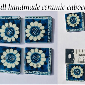 May include: Five handmade ceramic cabochons with a white flower design on a blue background. The cabochons are approximately 1 inch square.