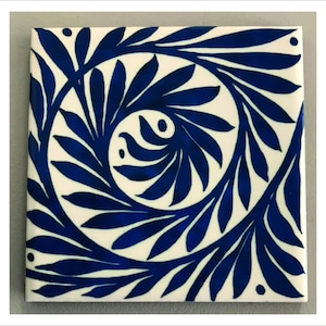 May include: A white ceramic tile with a blue floral design. The design features swirling leaves and branches.